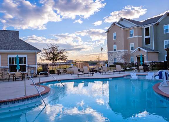 A swimming pool in front of a building with a sunset in the background.