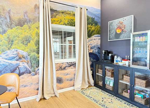 A room with a large mural of a landscape behind a window with beige curtains.