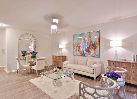 A living room with a white couch, a glass coffee table, and a painting on the wall.