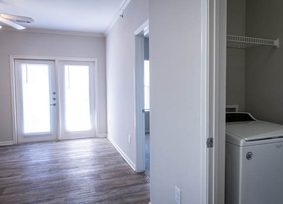 A white washing machine is in a small room with wood floors and white walls.