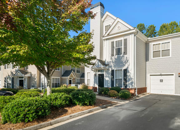 a white house with a driveway and a tree in front of it