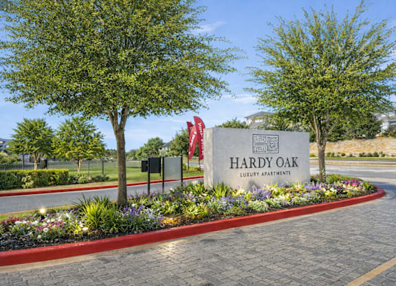 The image shows a sign for Hardy Oak Luxury Apartments surrounded by a well-manicured garden and trees.