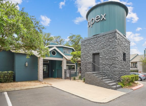 the entrance of apex apartments with a water tower and sign that says apex