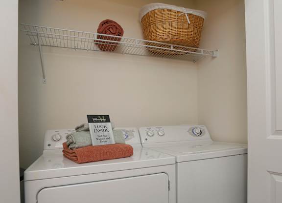 A small laundry room with a washer and dryer and a basket on the shelf.