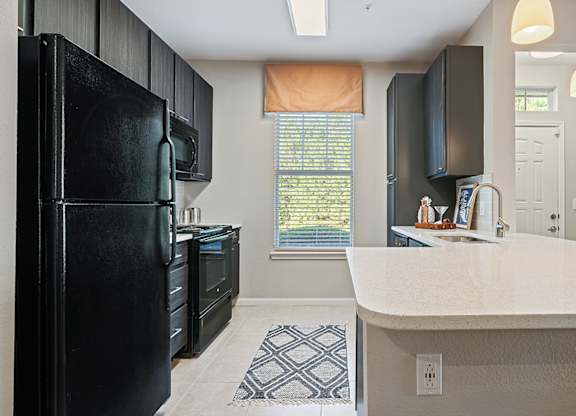 A black fridge in a kitchen with a white counter top.