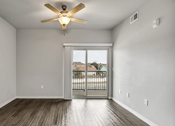 an empty living room with a ceiling fan and a door to a balcony