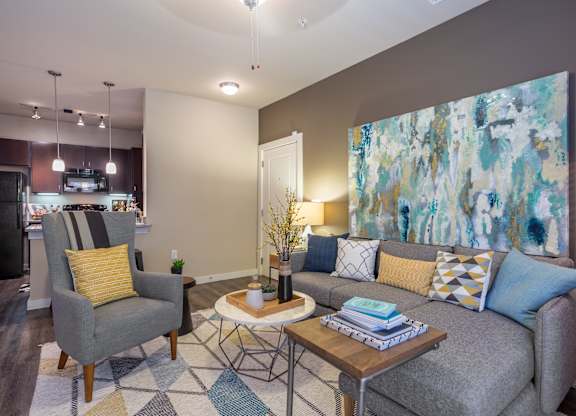 A living room with a grey couch, a yellow pillow, a grey armchair, a coffee table, and a painting on the wall.