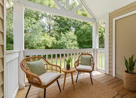 A white chair with a green pillow sits on a porch.