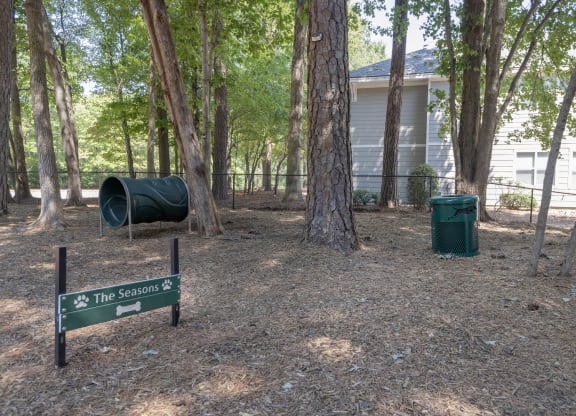 Bark park surrounded by trees with dog exercise equipment at  Seasons at Umstead apartments in Raleigh