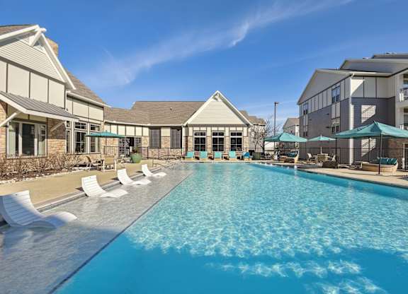 a swimming pool with chairs and umbrellas in front of a building with apartments