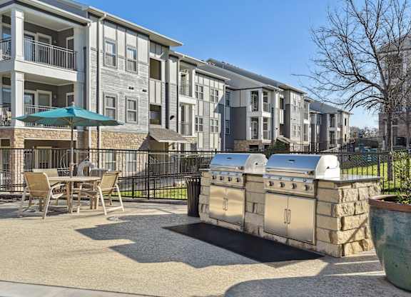 a patio with a grill and a table and chairs in front of an apartment building