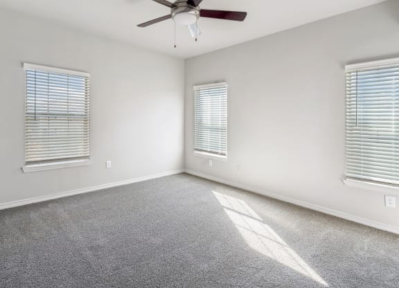 an empty living room with a ceiling fan and two windows