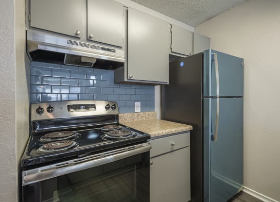 1 Bedroom Apartments in Duluth, GA - The Eclipse - Kitchen with Stainless Steel Appliances, Granite Countertops, Light Grey Cabinetry, Tile Backsplash, and Designer Wood Look Plank Flooring