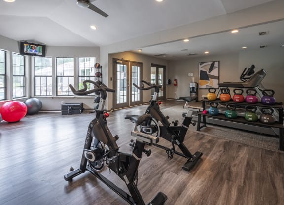 a modern apartment complex gym with weights and cardio equipment and windows