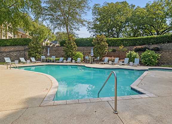 A swimming pool surrounded by trees and a stone wall.
