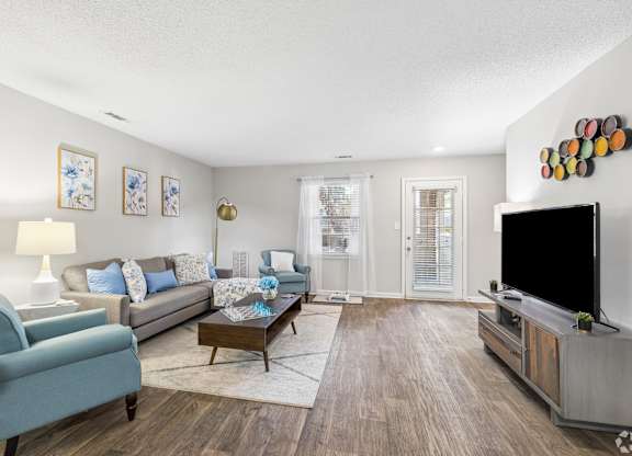A living room with a blue chair, a grey couch, a coffee table, a flat screen TV and a wall with pictures and a decoration.
