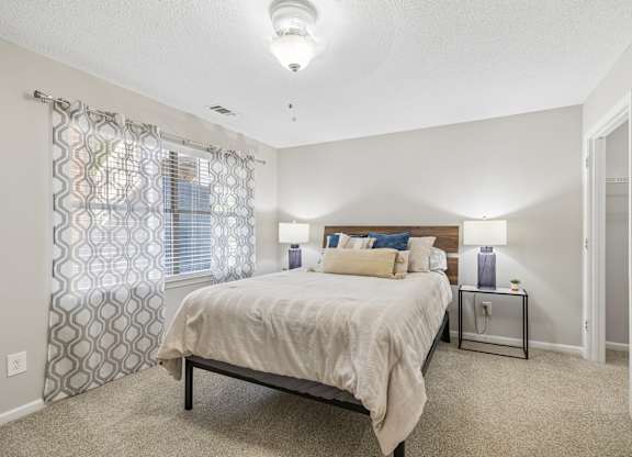 A bedroom with a bed, nightstand, and window with curtains.
