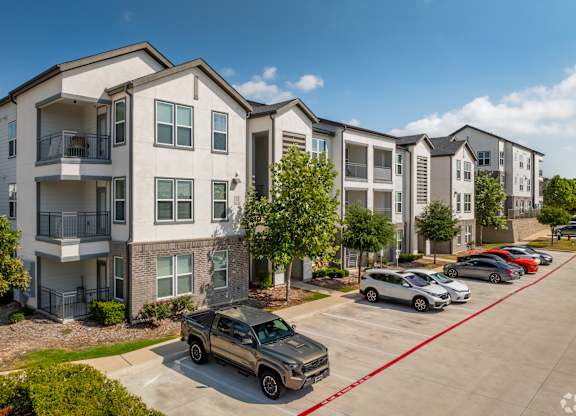 A row of apartment buildings with cars parked in front.
