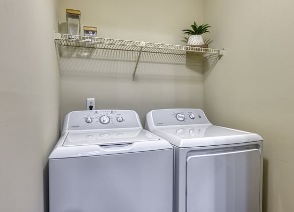 a washer and dryer in a laundry closer with a shelf above them at Wynnwood Vinings apartments