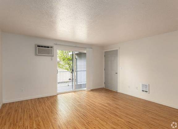 A room with wooden floors and white walls, with a sliding glass door leading outside.