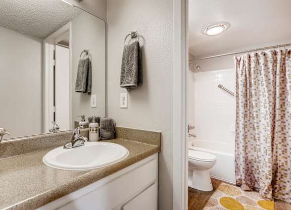 A bathroom with a sink, mirror, toilet, and shower at The Ranch at Bear Creek Apartments, Lakewood, 80227