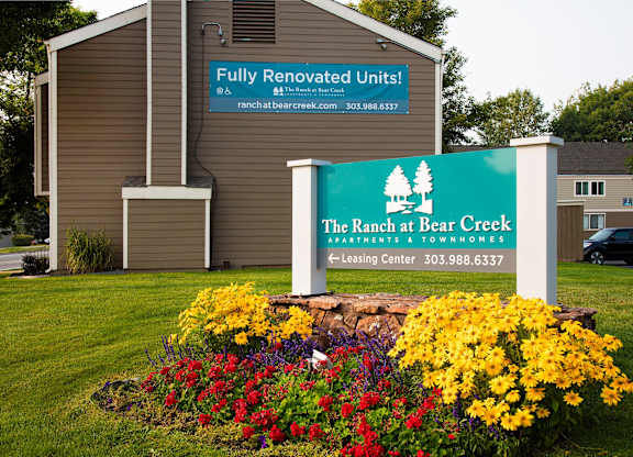 A sign for The Ranch at Bear Creek Apartments & Townhomes is displayed in front of a building.