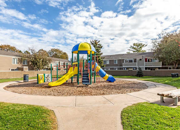 A playground with a yellow and blue slide in the middle of a grassy area at The Ranch at Bear Creek Apartments, Lakewood, CO