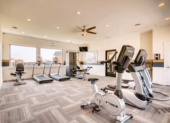 A gym with a variety of exercise equipment including treadmills, stationary bikes, and elliptical machines at Mountain Vista Apartments, Lakewood, 80228