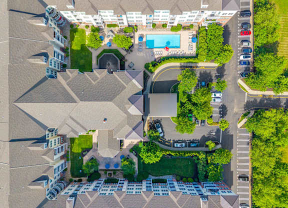 A bird's eye view of a residential area with houses, a swimming pool, and a parking lot.