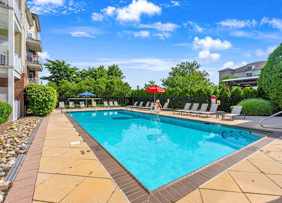 A swimming pool surrounded by a stone border and lounge chairs.