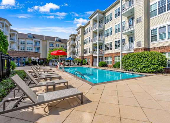 A pool area with sun loungers and a red umbrella in front of apartment buildings.