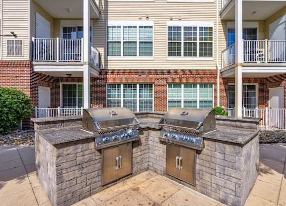Two outdoor BBQs are built into the side of a brick building.