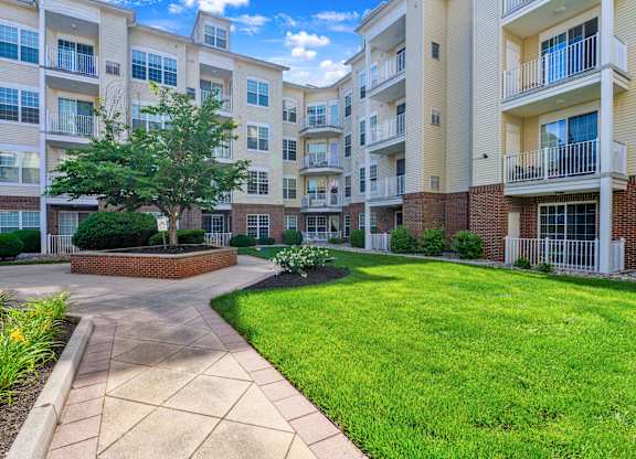 A sunny day at a brick apartment complex with a walkway and green grass.