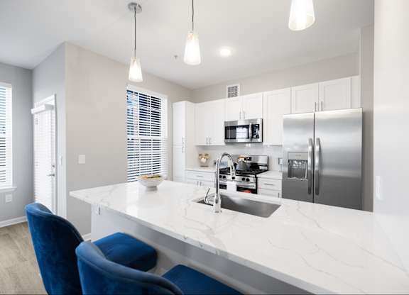A modern kitchen with a white countertop and blue chairs.