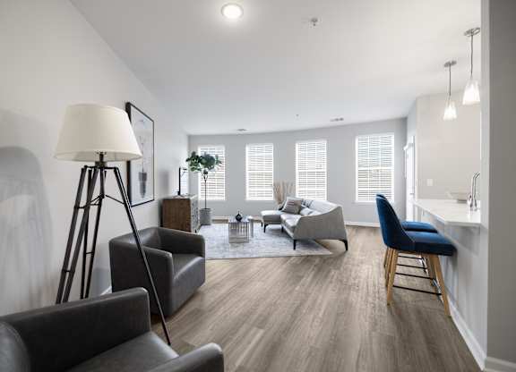 A well-lit living room with a grey sofa, a black chair, and a wooden floor.