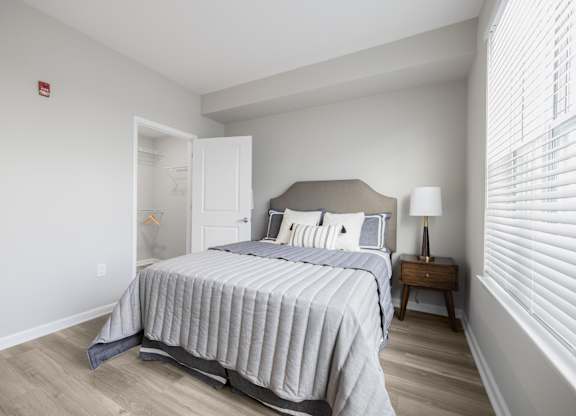 A bedroom with a bed, nightstand, and window with blinds.