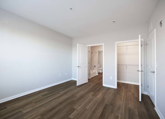 A room with white walls and wood flooring, with two open doors.