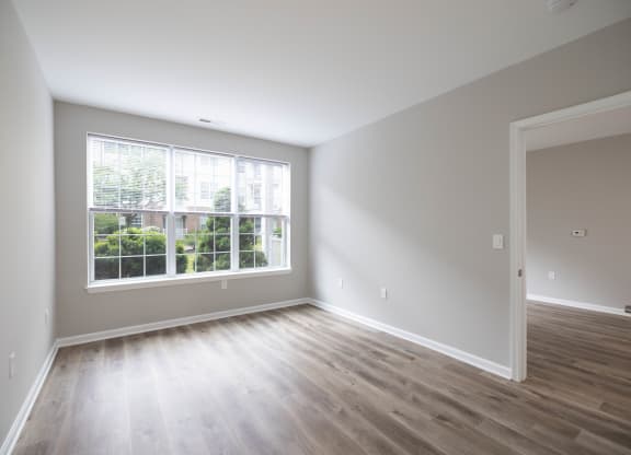 an empty living room and kitchen with white walls and wood flooring at The Lena, Raritan, NJ 08869