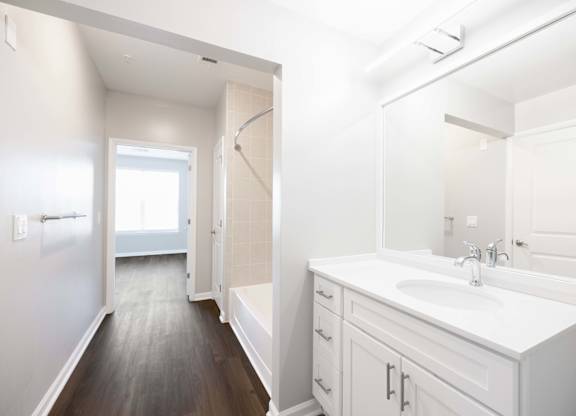 A white bathroom with a sink, mirror, and wooden floor.
