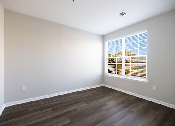 A room with wooden flooring and a window with blinds.