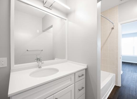 A white bathroom with a sink, mirror, and bathtub.
