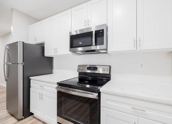 a kitchen with white cabinets and black appliances and a stainless steel refrigerator at The Lena, Raritan, NJ 08869