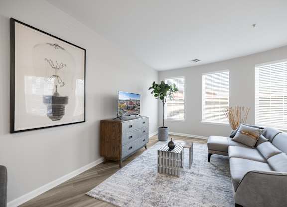 A living room with a grey sofa, a grey rug, a wooden cabinet, a side table, a potted plant, and a framed picture on the wall at Harbor Pointe Apartments, New Jersey