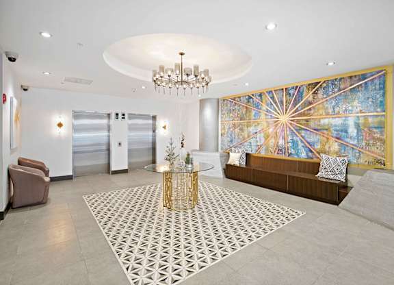 A large, modern living room with a chandelier, a sofa, a coffee table, and a large, colorful mural on the wall.