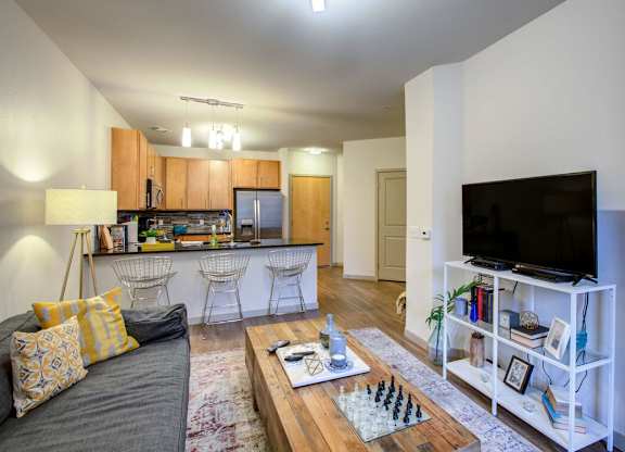 A modern living room with a grey couch, a wooden coffee table, and a flat screen TV on a white stand at Regatta Sloans Lake Apartments, Denver, CO