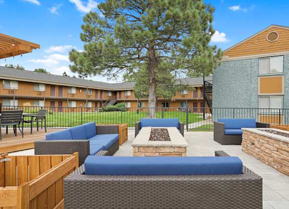 A large tree is in the middle of a patio with blue couches and wooden tables at Mountain Vista Apartments, Lakewood, CO