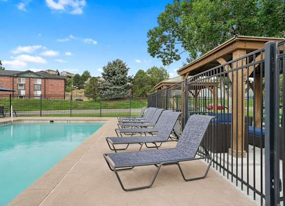 A pool with lounge chairs and a fence at Mountain Vista Apartments, Lakewood