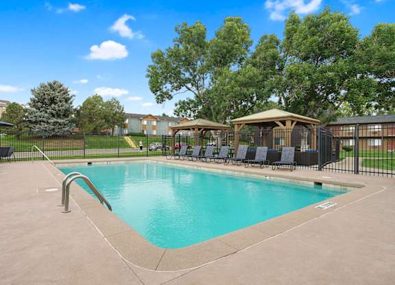 A swimming pool surrounded by a black fence and trees at Mountain Vista Apartments, Lakewood, 80228