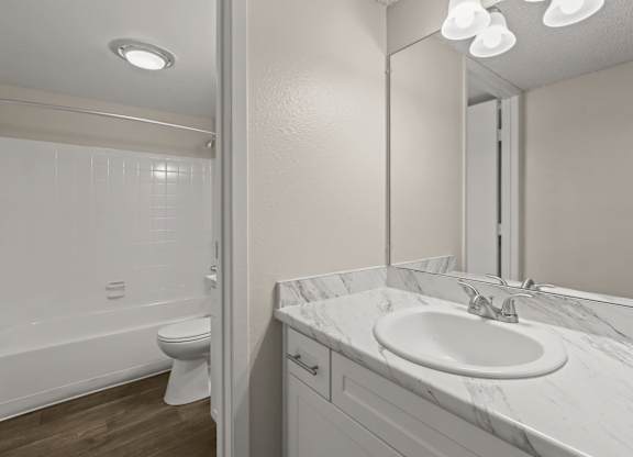 A white bathroom with a toilet, sink, and mirror at The Ranch at Bear Creek Apartments, Lakewood, CO, 80227