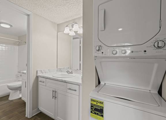 A white washing machine is in a laundry room with a sink and mirror at The Ranch at Bear Creek Apartments, Colorado, 80227